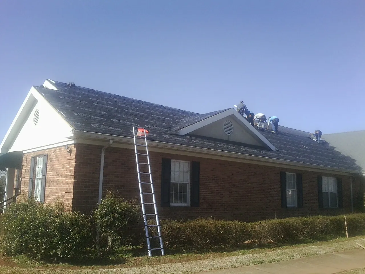 Crew tearing shingles off a brick ranch roof with a ladder set — Metal Roof Repair work by our crew in Lakeside